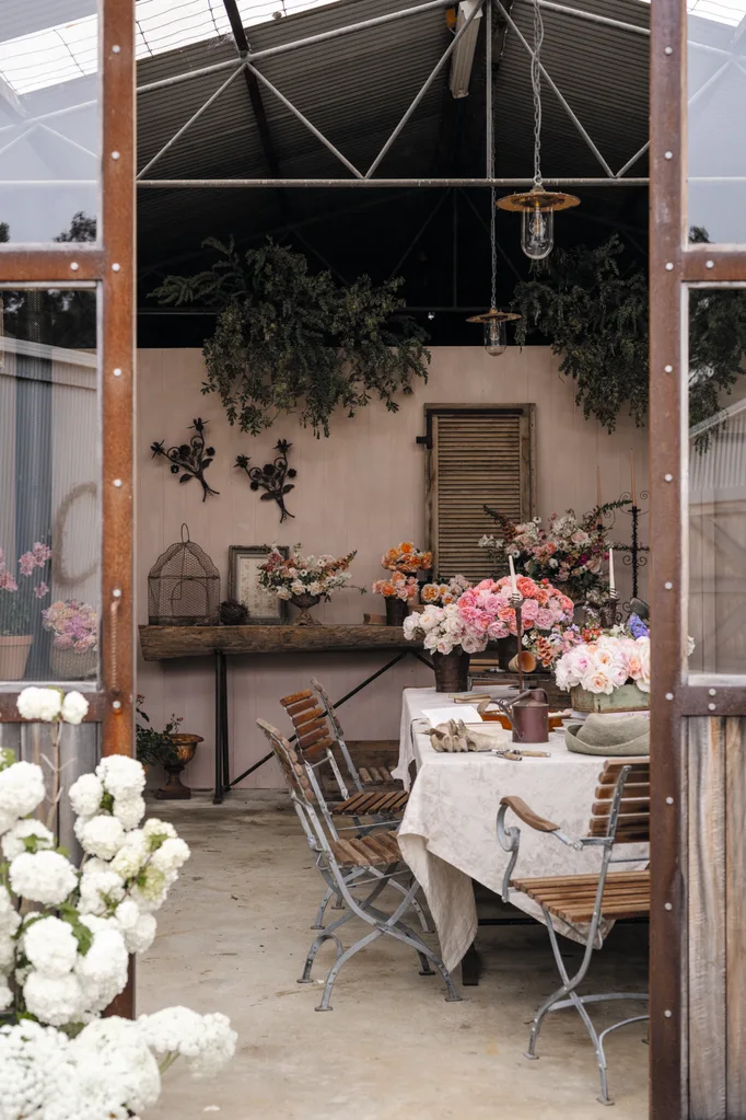 Floral workshop situated within a converted farm shed with a table, chairs, and vibrant flower arrangements under a rustic metal roof.