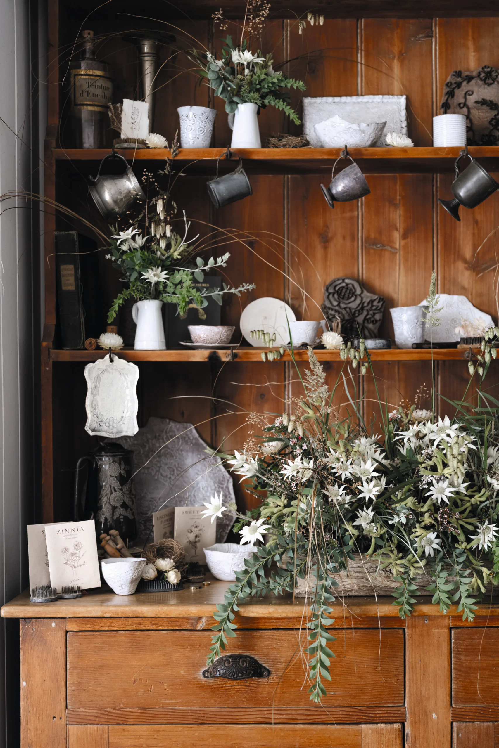 Wooden shelf with vintage decor, cups, vases, and lush floral arrangement with white flowers and green leaves.