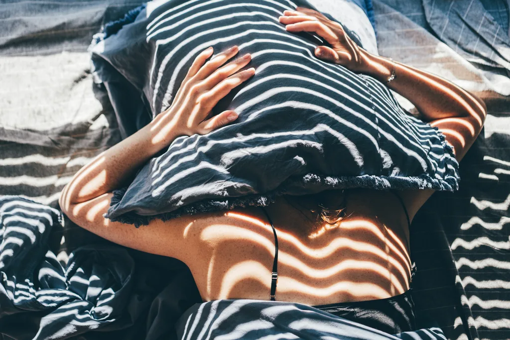 Sad and depressed woman lying in bed at home.