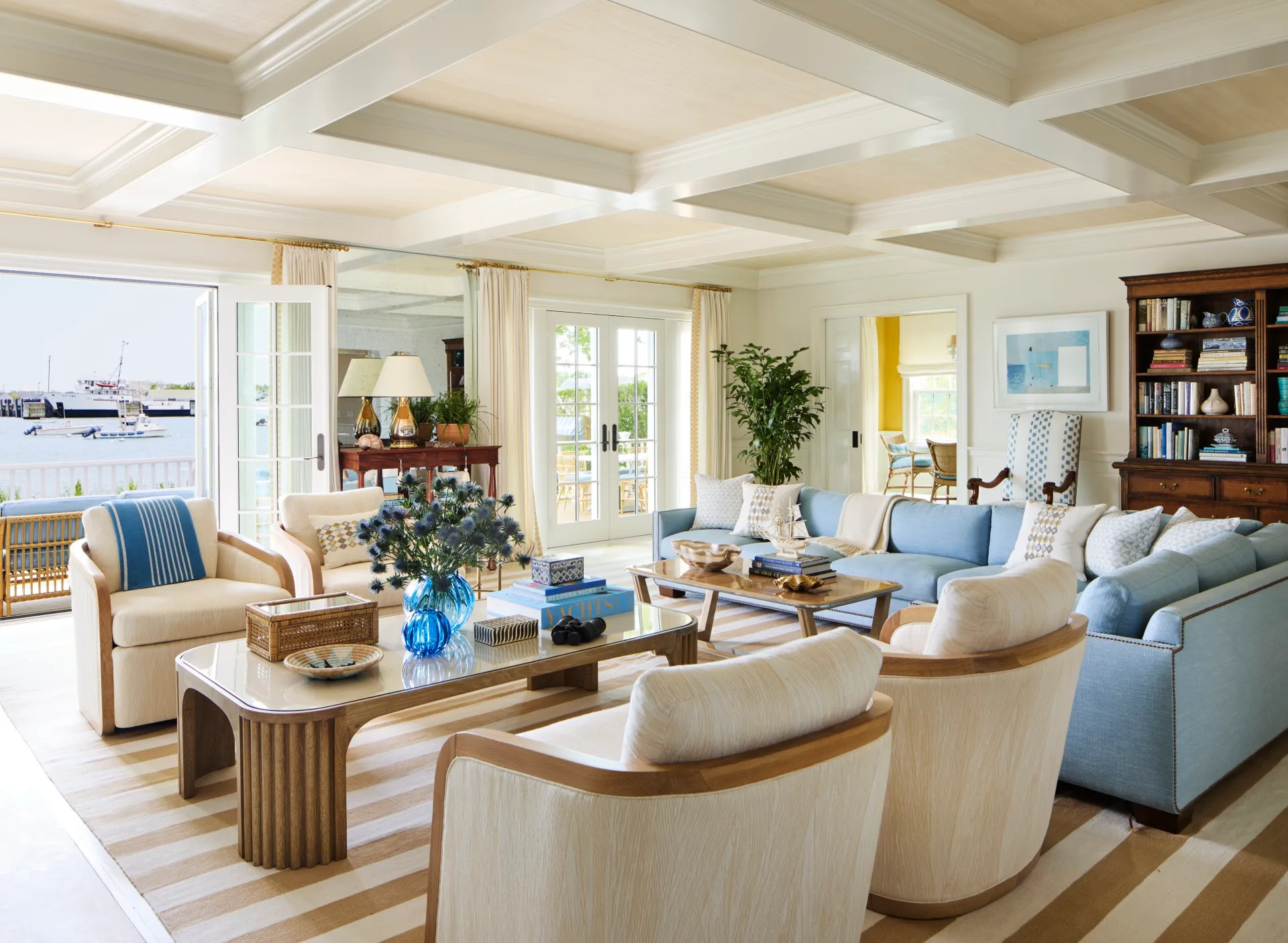 Coastal living room with blue and beige decor, large windows, and a view of the water.