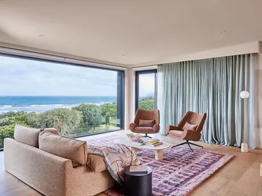 A living room with furniture that doesn't match with a different pink armchairs and sofa, a marble coffee table and maroon and pink rug.
