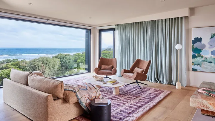 A living room with furniture that doesn't match with a different pink armchairs and sofa, a marble coffee table and maroon and pink rug.