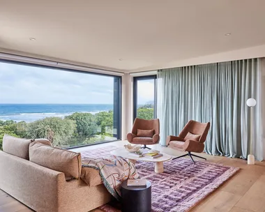 A living room with furniture that doesn't match with a different pink armchairs and sofa, a marble coffee table and maroon and pink rug.