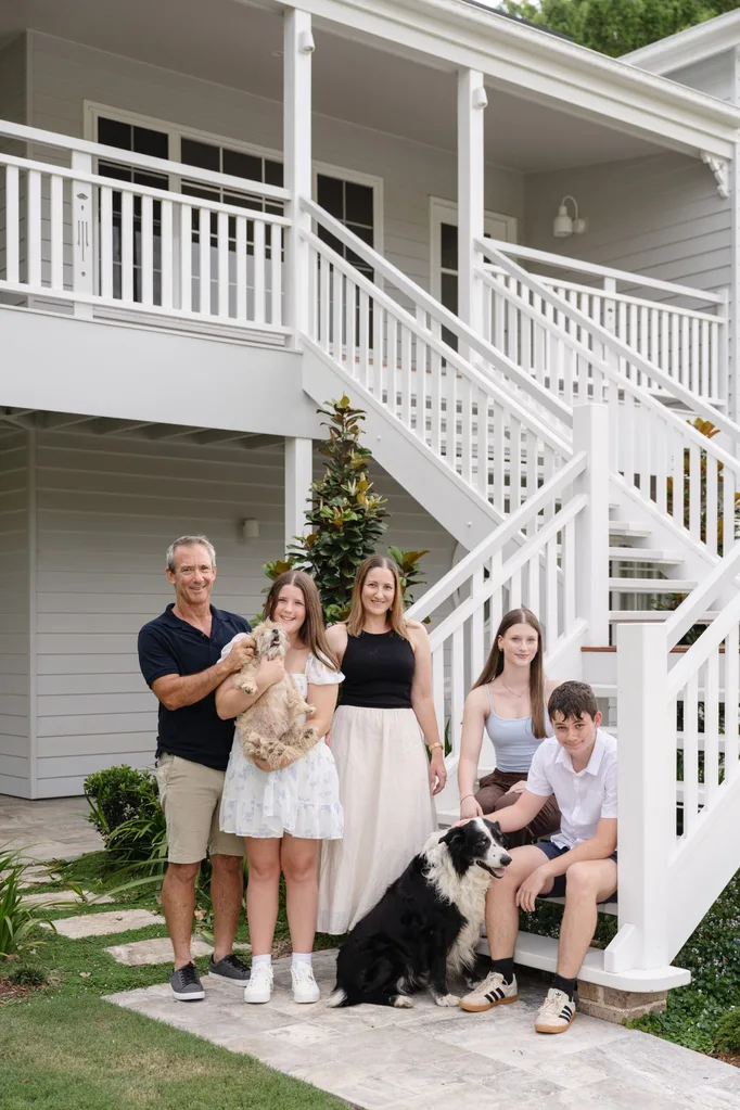 Front house clear mountain family members Nathan, Macey (holding Tess, the Maltese cross), Belinda, Ellie, Tyler and Charlie, the Border Collie, gather at the bottom of the entry staircase.
