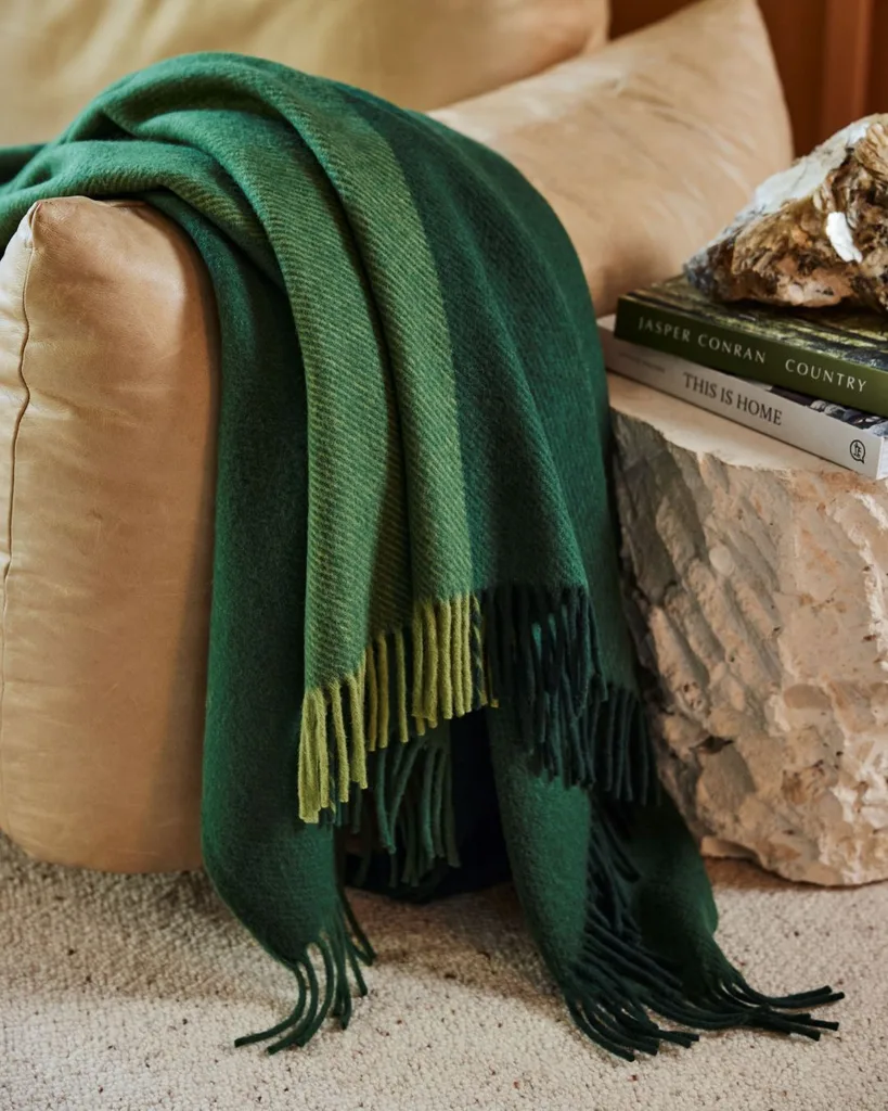 A quality wool blanket by Waverley Mills is various shades of green draped over a beige leather arm chair