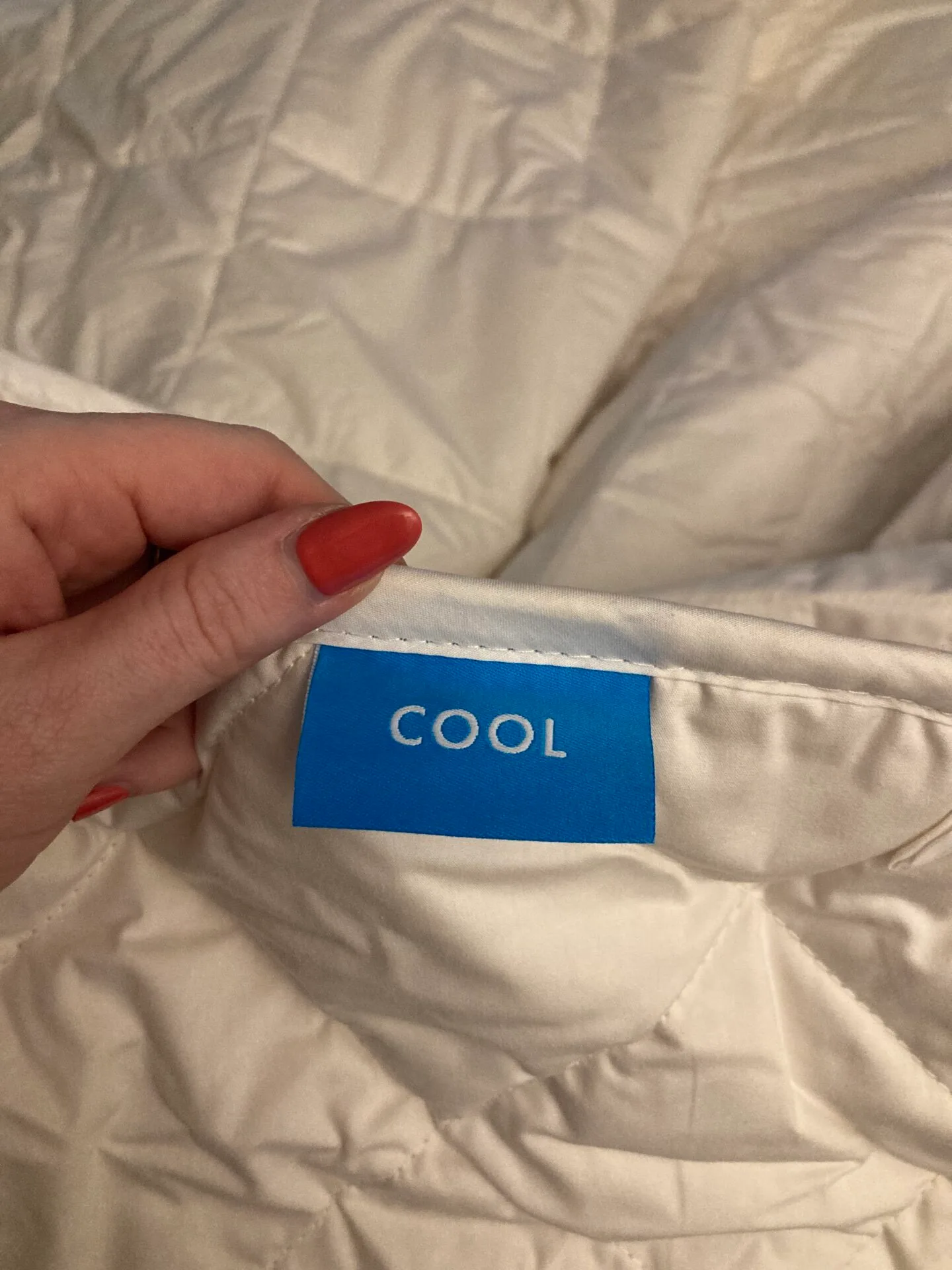 A close up photo of a quilt, with a label that says 'cool', held in place by a hand.