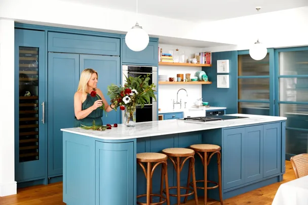 Wendy Moore in a blue kitchen arranging colourful flowers