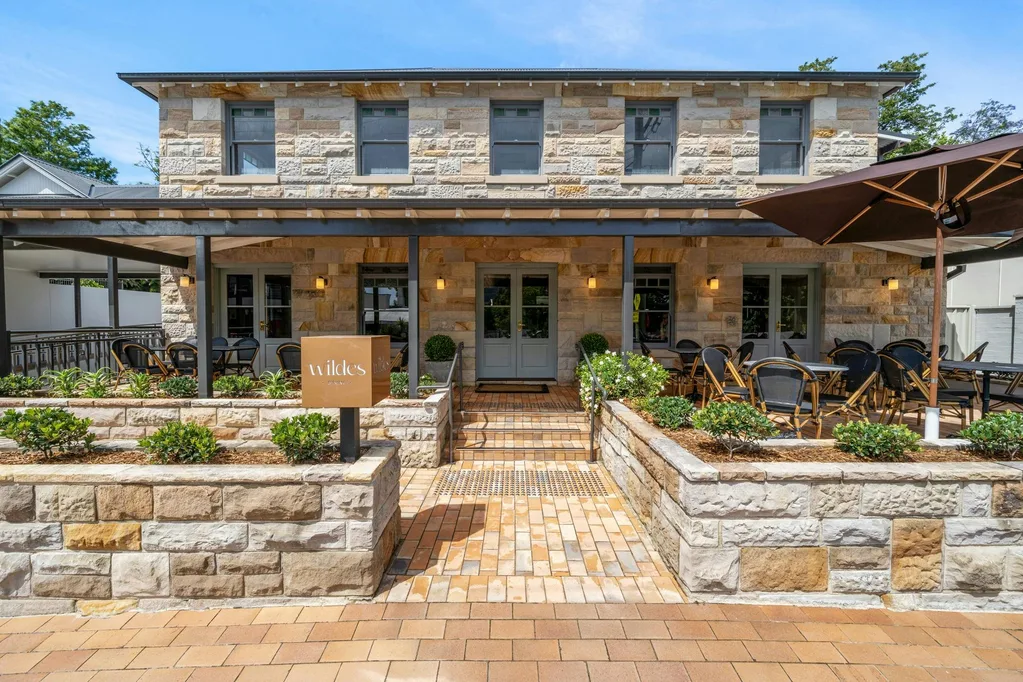 Front view of a stone building with outdoor seating and a sign reading "Wilde's."