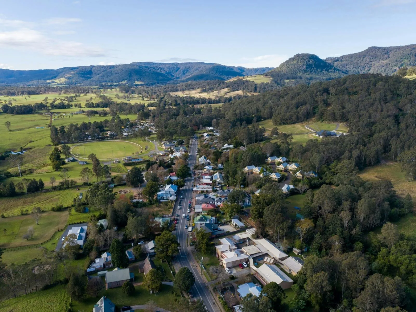 Aerial view of a small rural town Kangaroo Valley with surrounding green fields and hills under a blue sky.