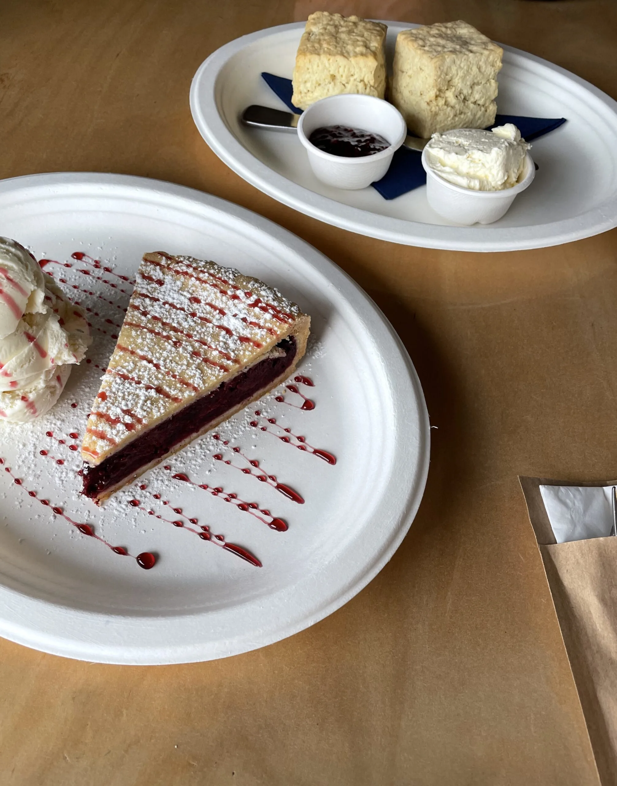 Slice of berry pie with ice cream and scones with jam and cream on plates