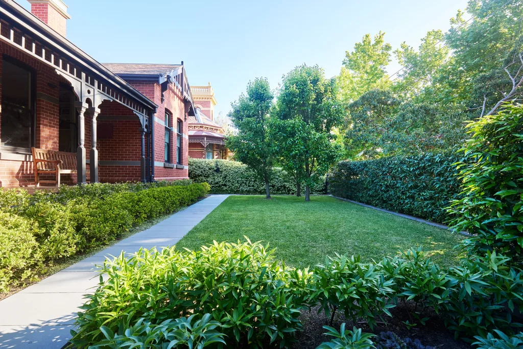 Formal front garden of a Federation-era Melbourne home with clipped hedges, ornamental pear trees and a neat lawn.