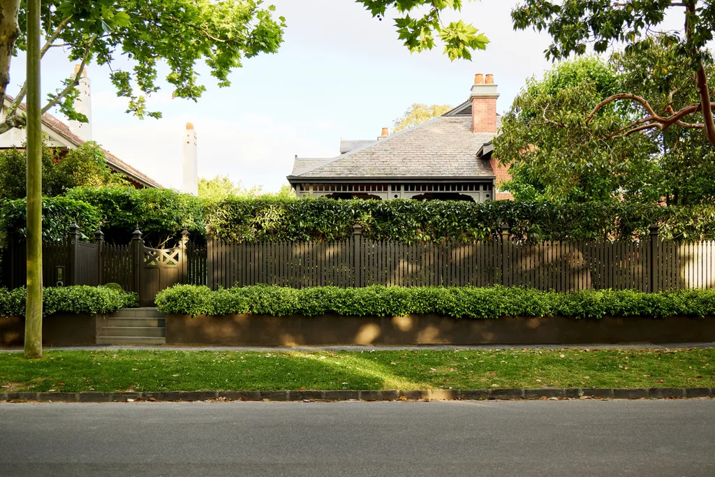 Federation-era Melbourne home hidden behind a traditional timber picket fence, clipped hedges and mature trees.