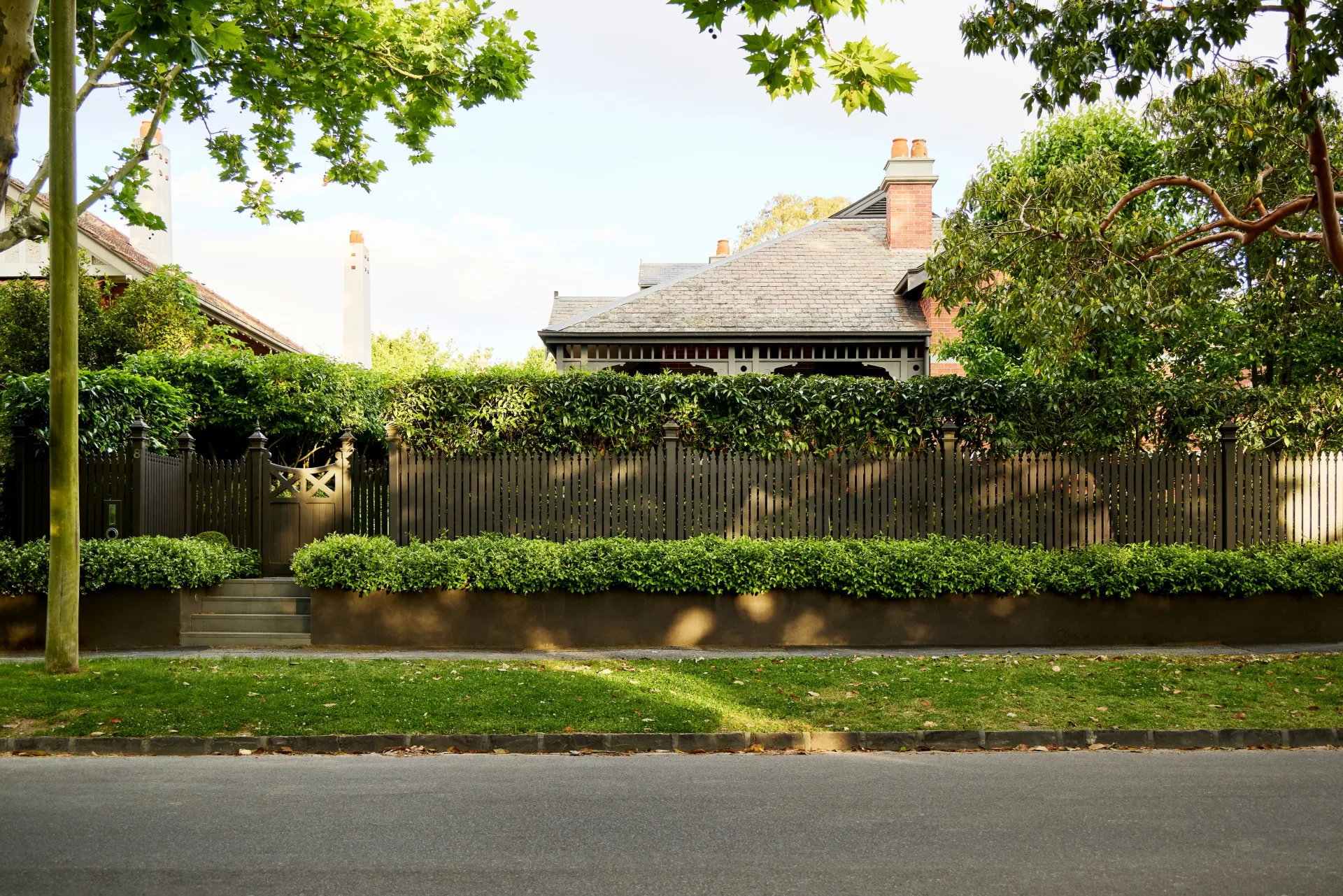 Federation-era Melbourne home hidden behind a traditional timber picket fence, clipped hedges and mature trees.