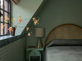 A cozy colour-drenched on-trend bedroom in 2026 with green walls, window seat with flowers, lamp on side table, and arched headboard.