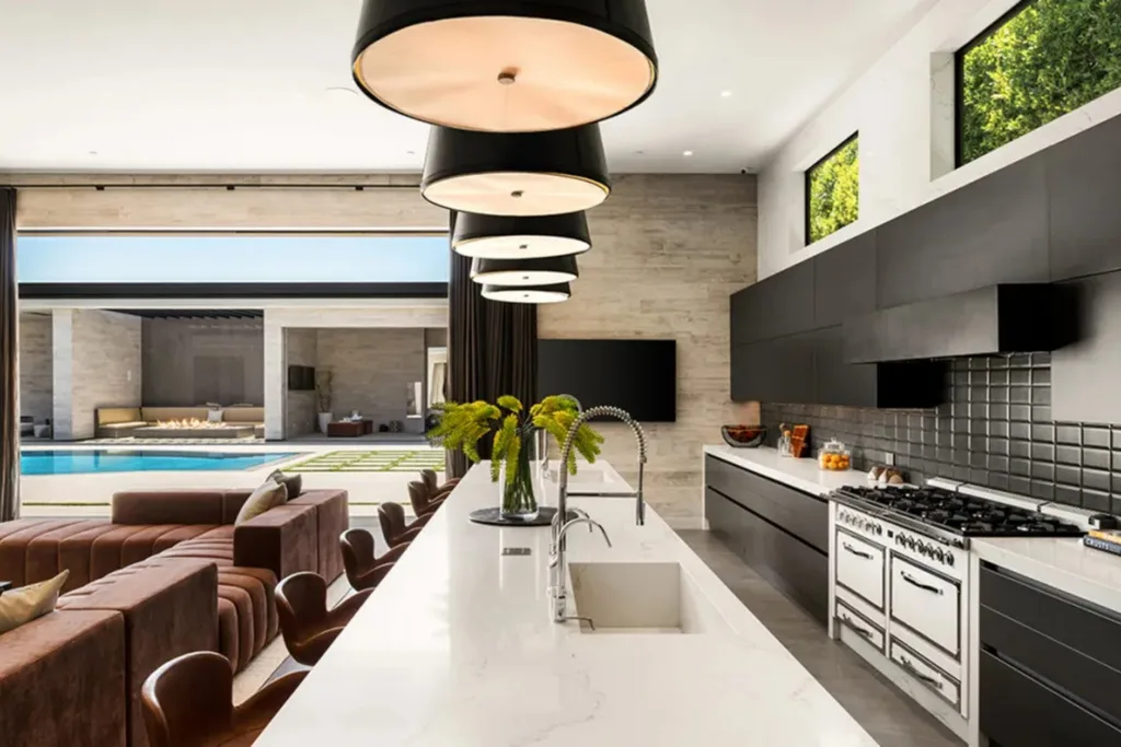 Large modern kitchen inside Kylie Jenner’s Los Angeles home with black cabinetry, white island bench and oversized pendant lights.