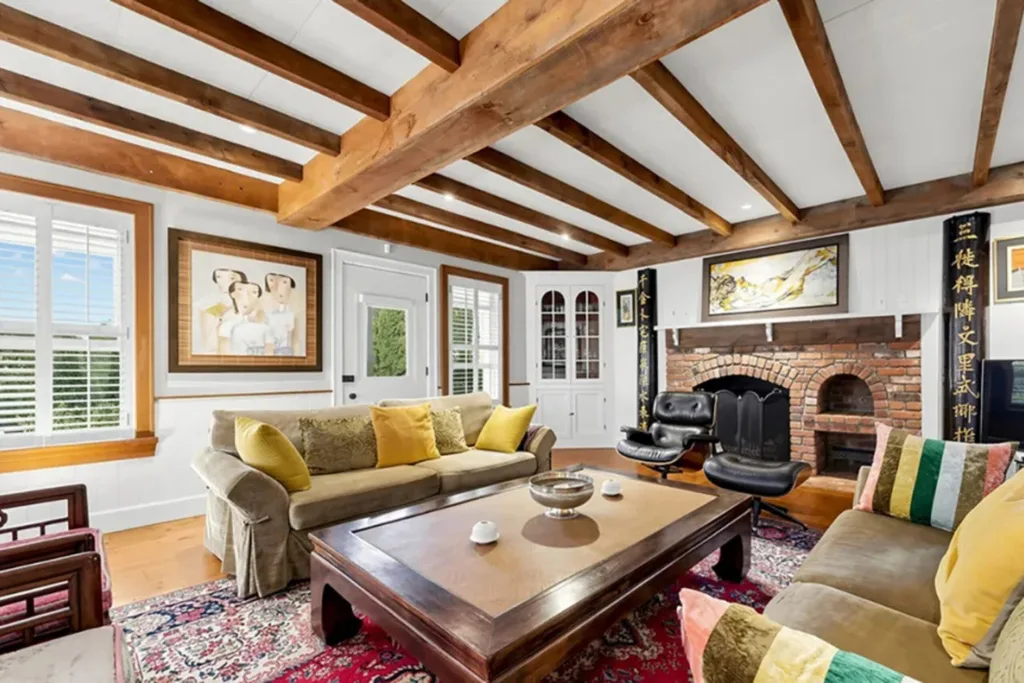 Living room with exposed timber ceiling beams, brick fireplace, timber floors and cosy seating.