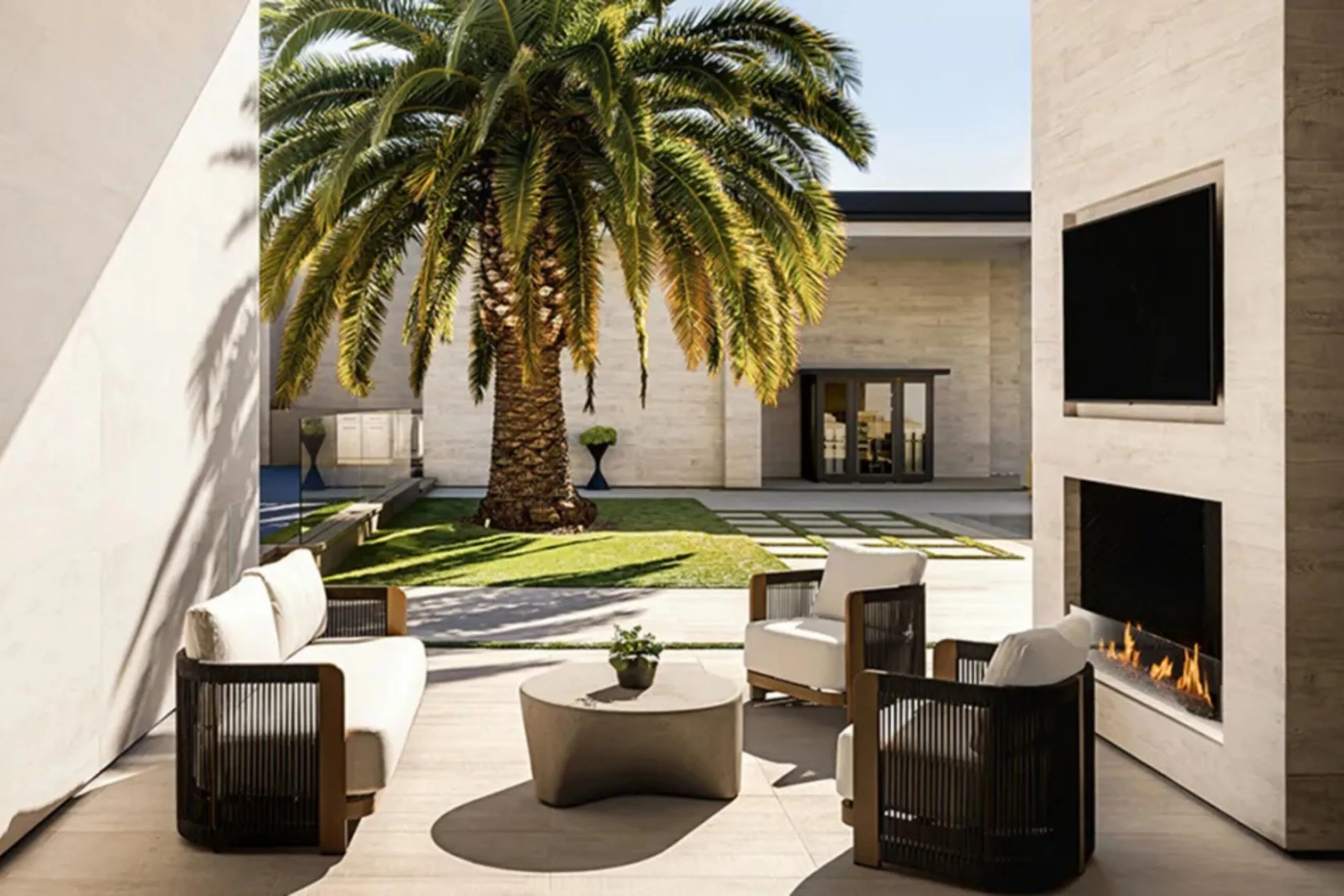 Outdoor entertaining area at Kylie Jenner&rsquo;s Holmby Hills home with fireplace, seating and large palm tree.