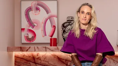 An image of Claudia lambert in a purple top against a pink purple colour scheme, including pink marble fireplace and pink and purple abstract contemporary artwork.