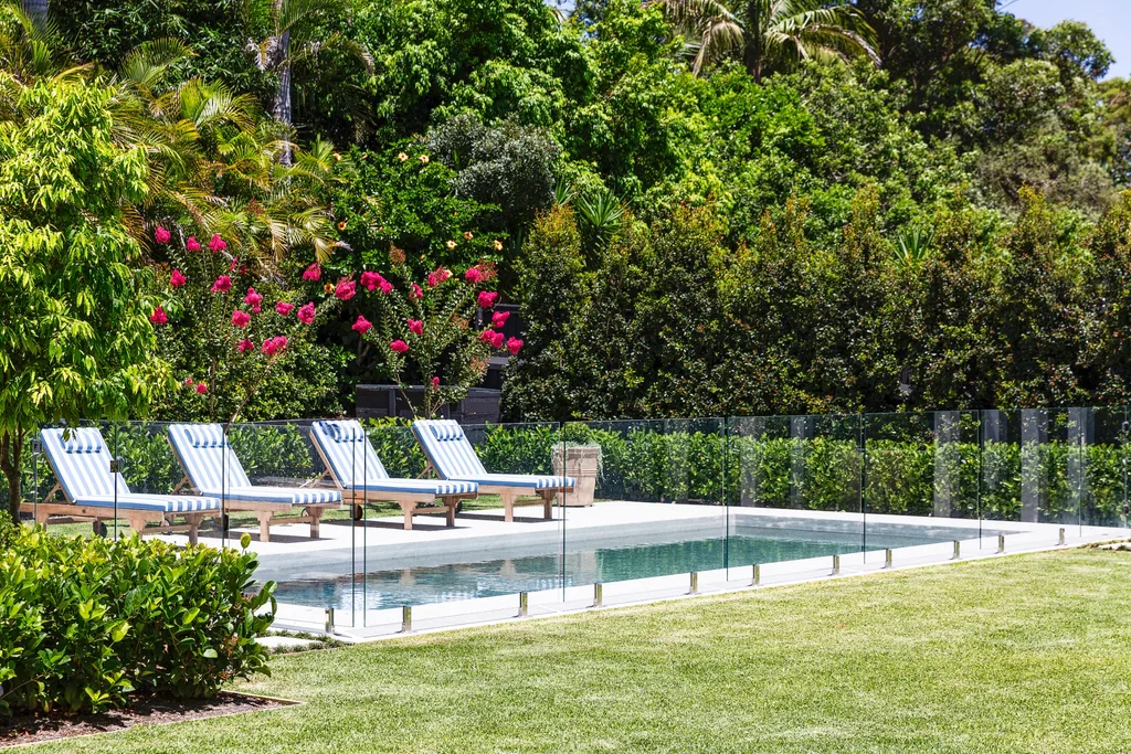 Poolside area with four striped lounge chairs, glass fencing, and lush green foliage in the background. The quick-growing hedging plant, viburnum, borders the pool.