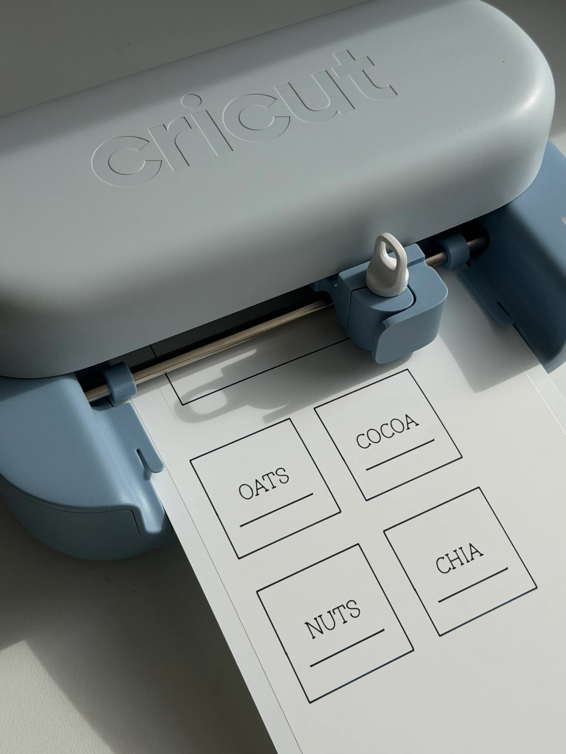 Cricut machine printing labels for oats, cocoa, nuts, and chia seeds.