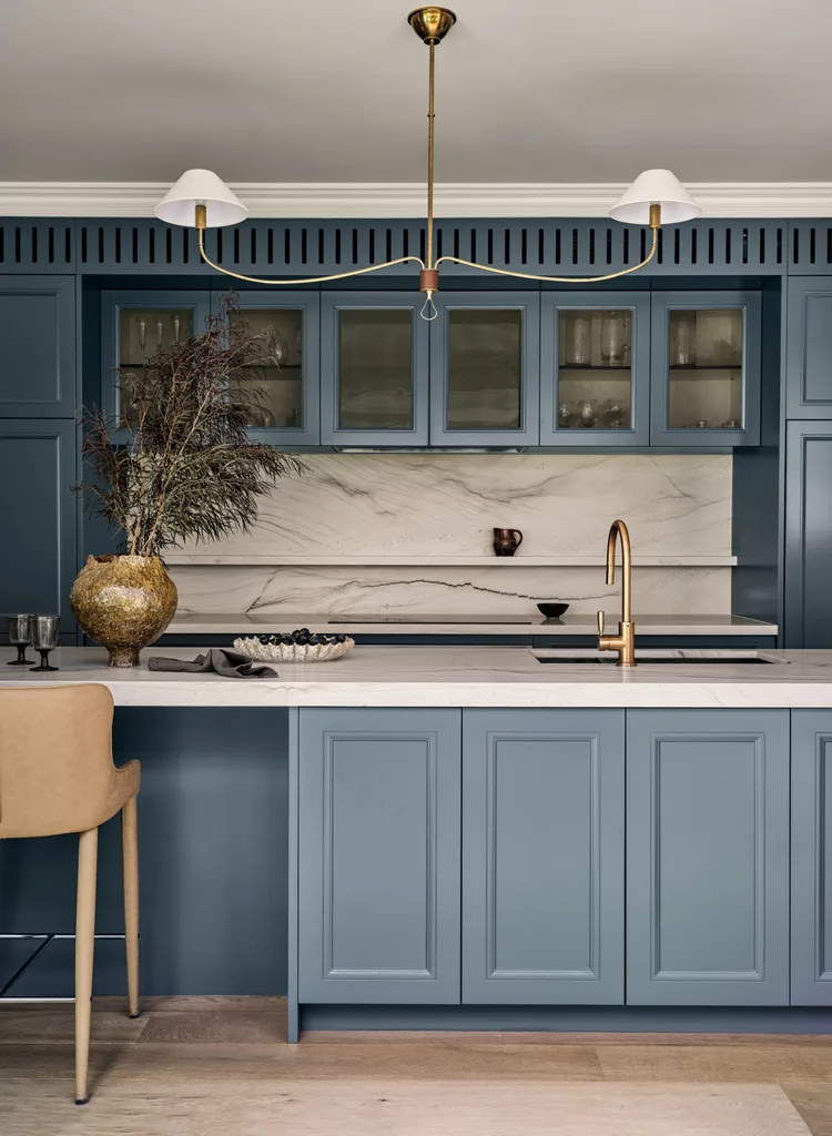 A large family kitchen that balances the latest kitchen trends with a sense of timelessness. The joinery profiles are finished in a shade of blue that is a bold contrast to the white ceilings, white marble benchtops and splashback and also the light toned timber flooring. Brass tapware is on the sink (built into the kitchen island) and a pendant light above the island is brass.