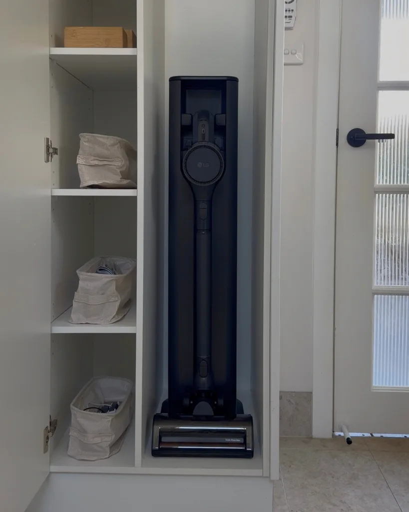 LG cordless vacuum cleaner neatly stored in a cabinet with shelves, near a door with a black handle.