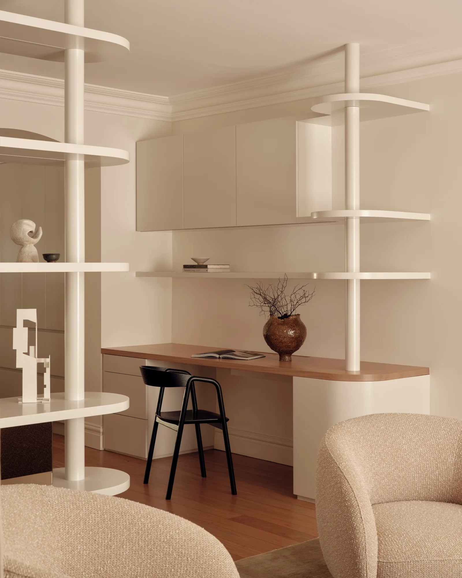 Minimalist home office with a wooden desk, black chair, decorative shelves, and neutral-toned furnishings.