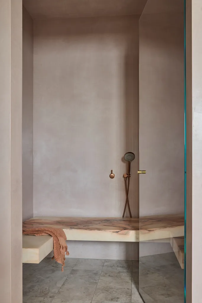 Minimalist modern 2026 shower room with taupe blush walls, marble bench, brown towel, and bronze fixtures.