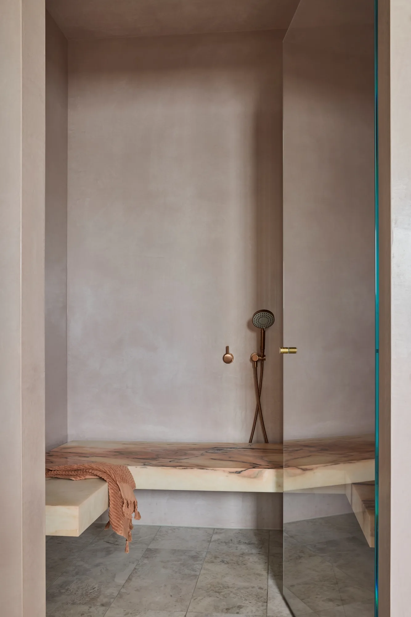Minimalist modern 2026 shower room with taupe  blush walls, marble bench, brown towel, and bronze fixtures.