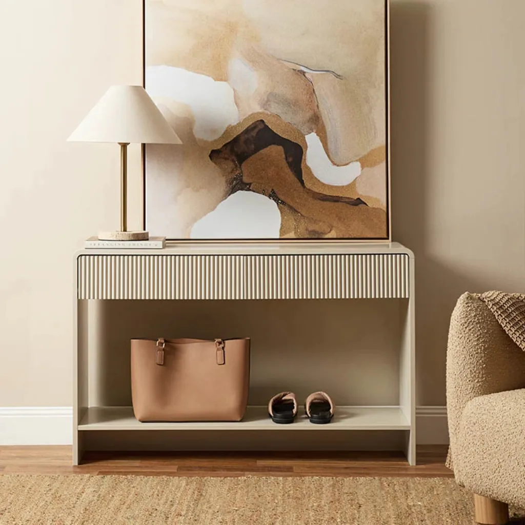 White beige console table with ridged detailing beneath top and shoes resting on the lower shelf