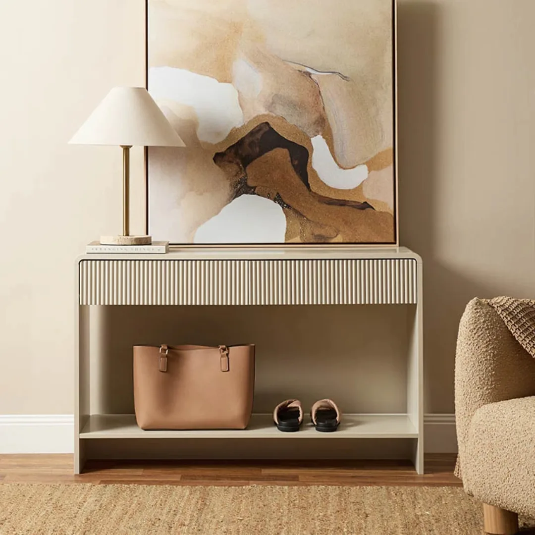 White beige console table with ridged detailing beneath top and shoes resting on the lower shelf