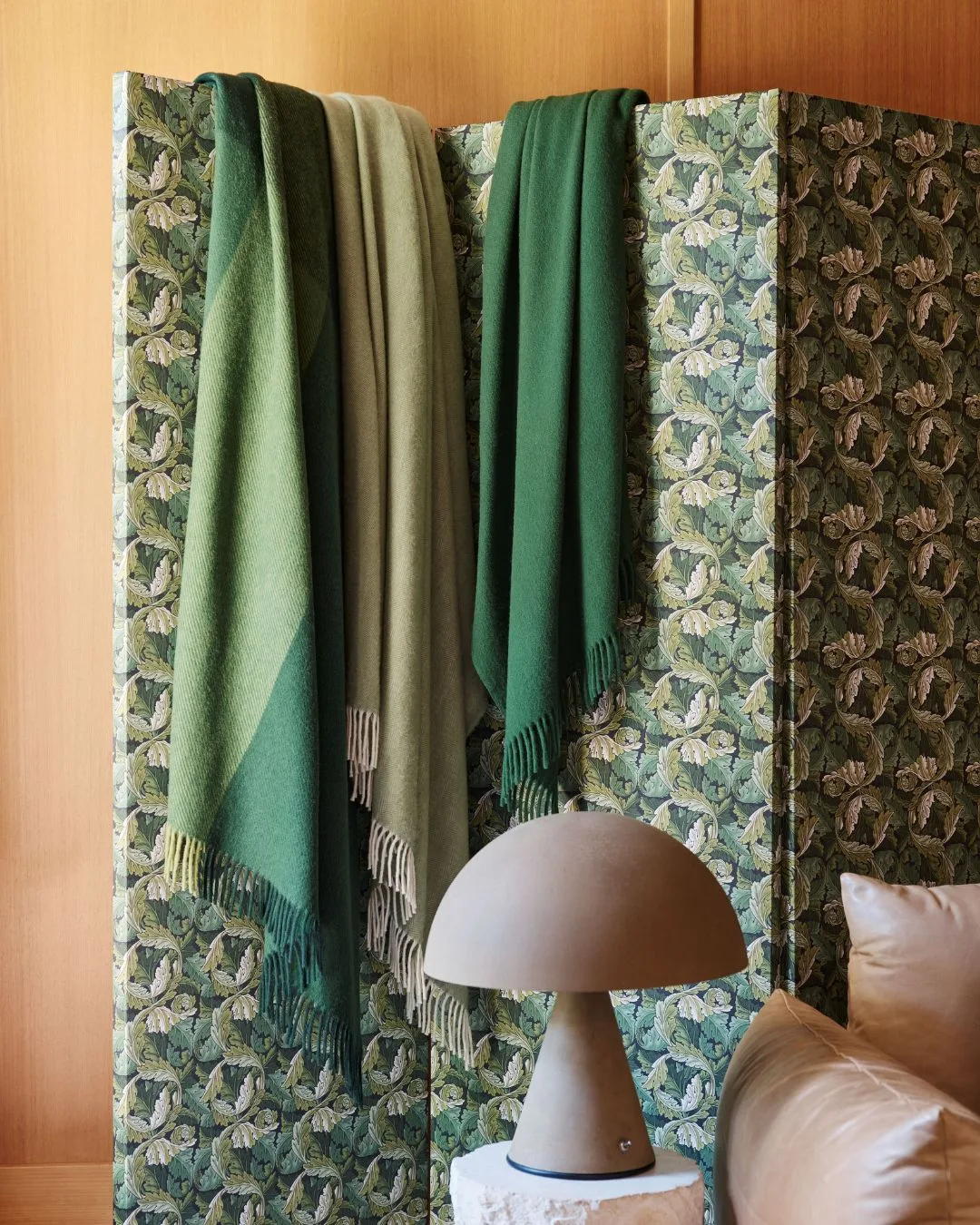 three Australian made wool blankets in various shades of green hung over a folding screen upholstered in a patterned green fabric.