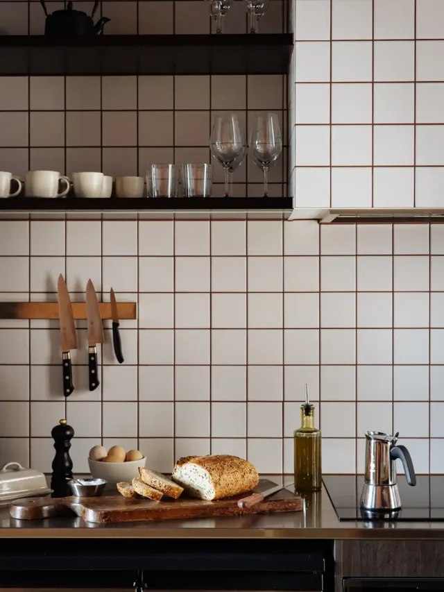 The kitchen space at Ogee Guesthouse Airbnb in Tasmania, featuring white square tile backsplash, cups, Japanese knives, and a fresh loaf of bread on the countertop.