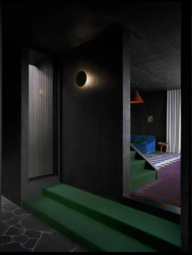 A hallway in Slow Beam, an architect-designed Airbnb in Tasmania with modern brightly coloured furniture and rugs contrasted against low lighting and black walls.
