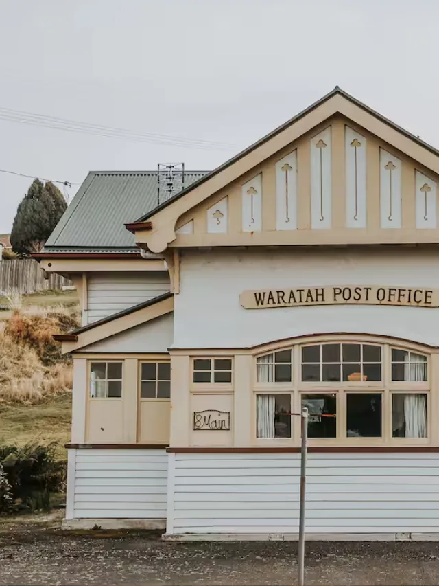 The outside of the Waratah Post Office Airbnb in Tasmania, painted in shades of yellow and cream and with a vintage sign out front.