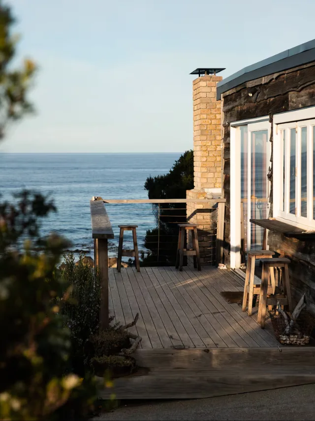 The outside deck of Whale Song Airbnb in Tasmania, with sweeping ocean views and lush shrubbery framing the image 
