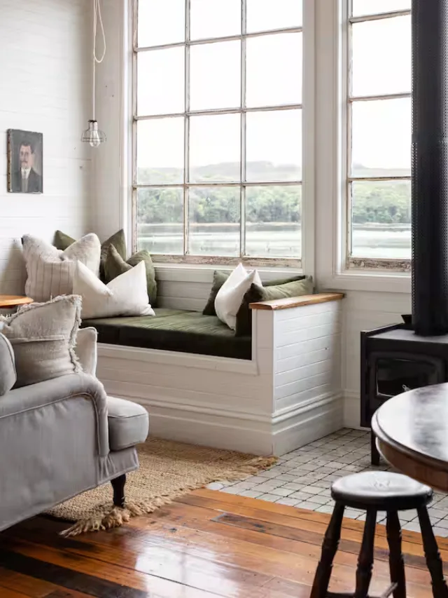 The living room of Captain's Rest, a boutique Airbnb in Strahan with a wood burning fireplace and ornate vintage furnishings arranged in front of a tall window with pier views
