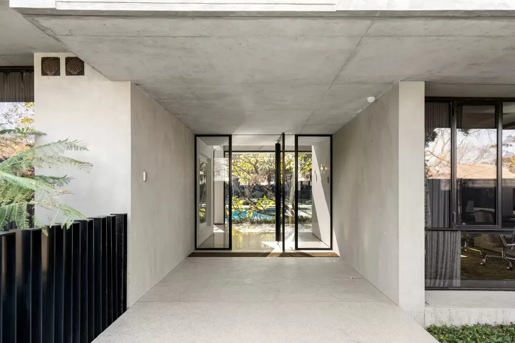 Concrete entrance to the Bali Body founders' Brighton home with black-framed glass doors and a view towards the pool. Bali Body founders' Brighton home