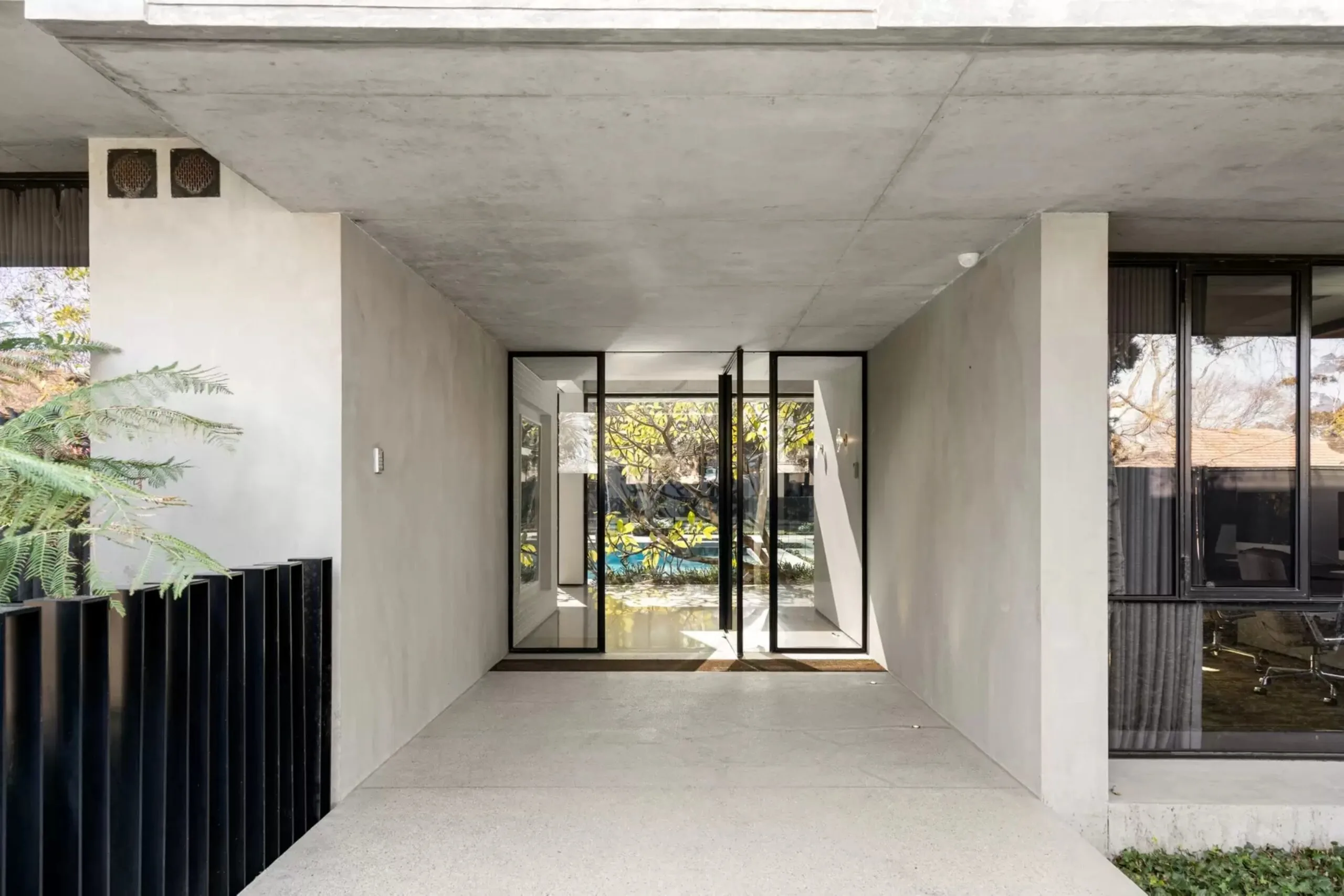 Concrete entrance to the Bali Body founders' Brighton home with black-framed glass doors and a view towards the pool. Bali Body founders' Brighton home