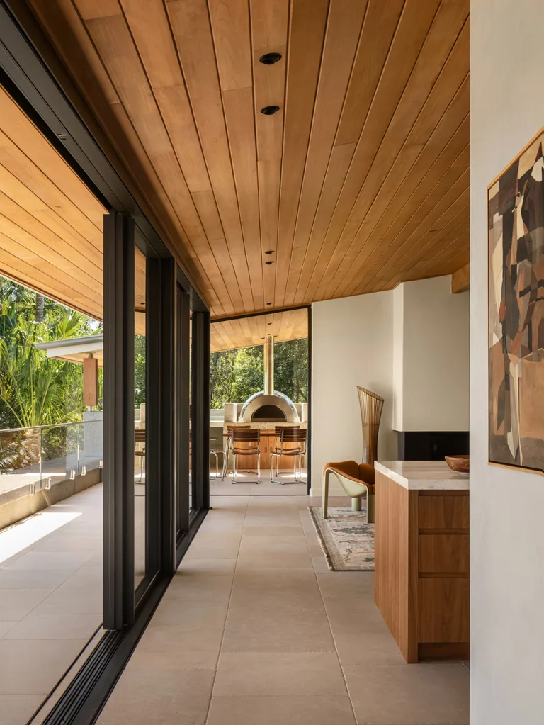Modern interior with wooden ceiling, large glass doors, and outdoor pizza oven. Harmonious blend of indoor and outdoor spaces.