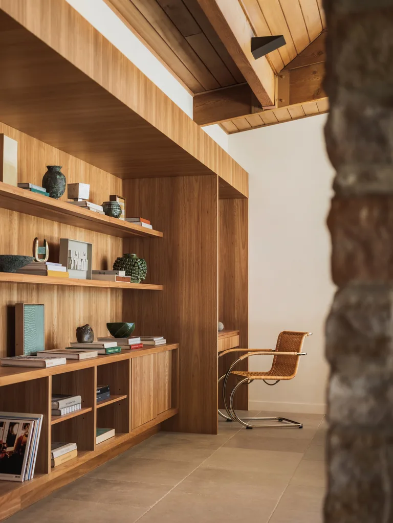 Warm, minimalist room with wooden shelves, books, decorative items, and a wicker chair, creating a cozy atmosphere.