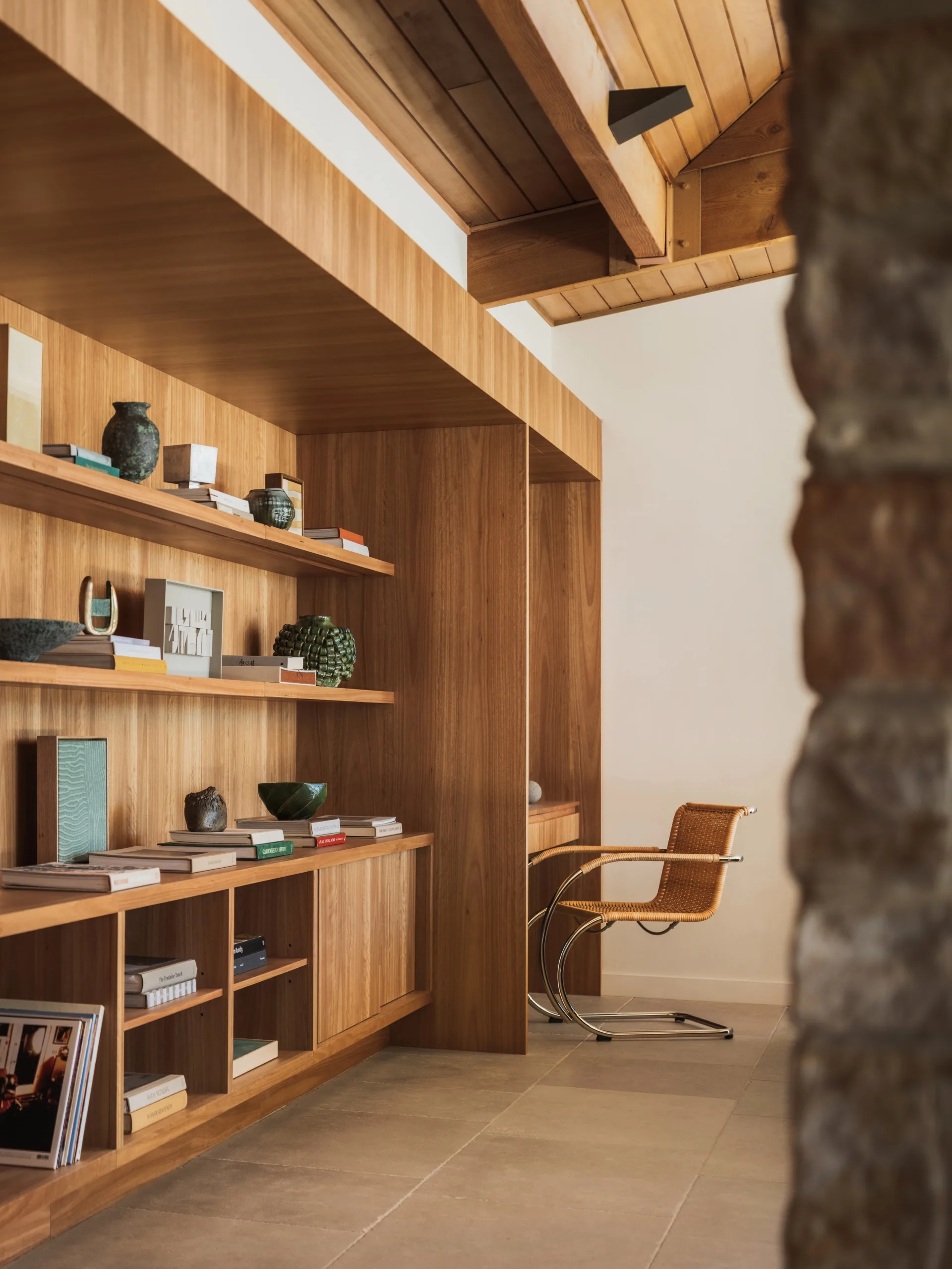 Warm, minimalist room with wooden shelves, books, decorative items, and a wicker chair, creating a cozy atmosphere.