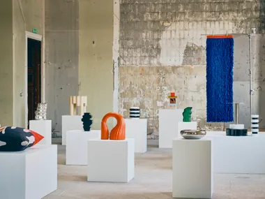 IKEA KONSTRUNDA sculptures, vessels, cushions and colourful textile artworks arranged on white plinths in an industrial gallery setting