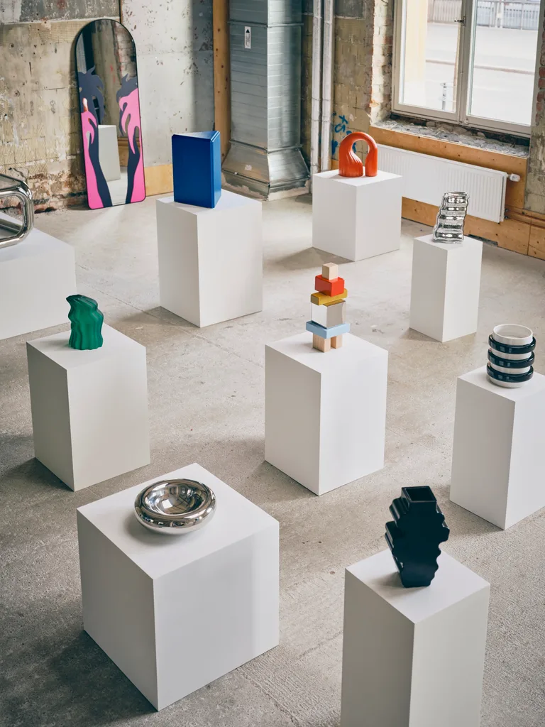 Colourful sculptures and decorative objects from the IKEA KONSTRUNDA collection displayed on white plinths in an industrial gallery space.