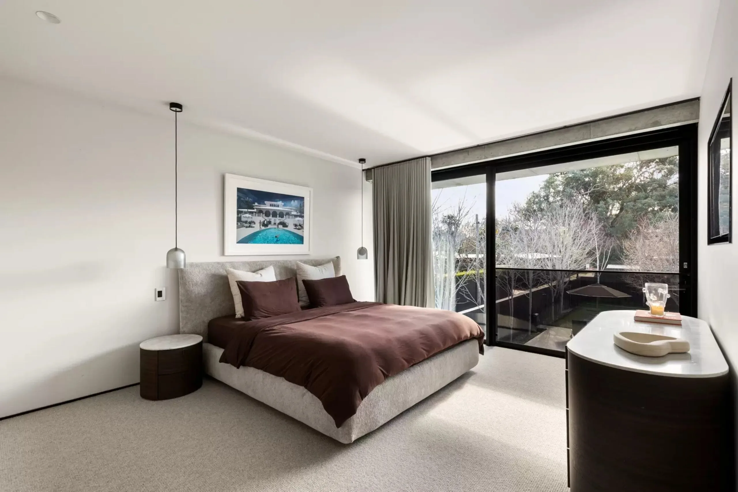 Bedroom with brown bedding, neutral carpet and large windows overlooking the garden.