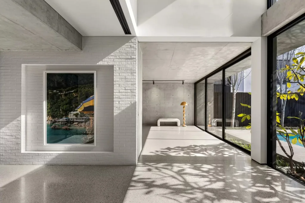 Light-filled interior with polished floors, white brick wall, artwork and floor-to-ceiling windows overlooking the garden.