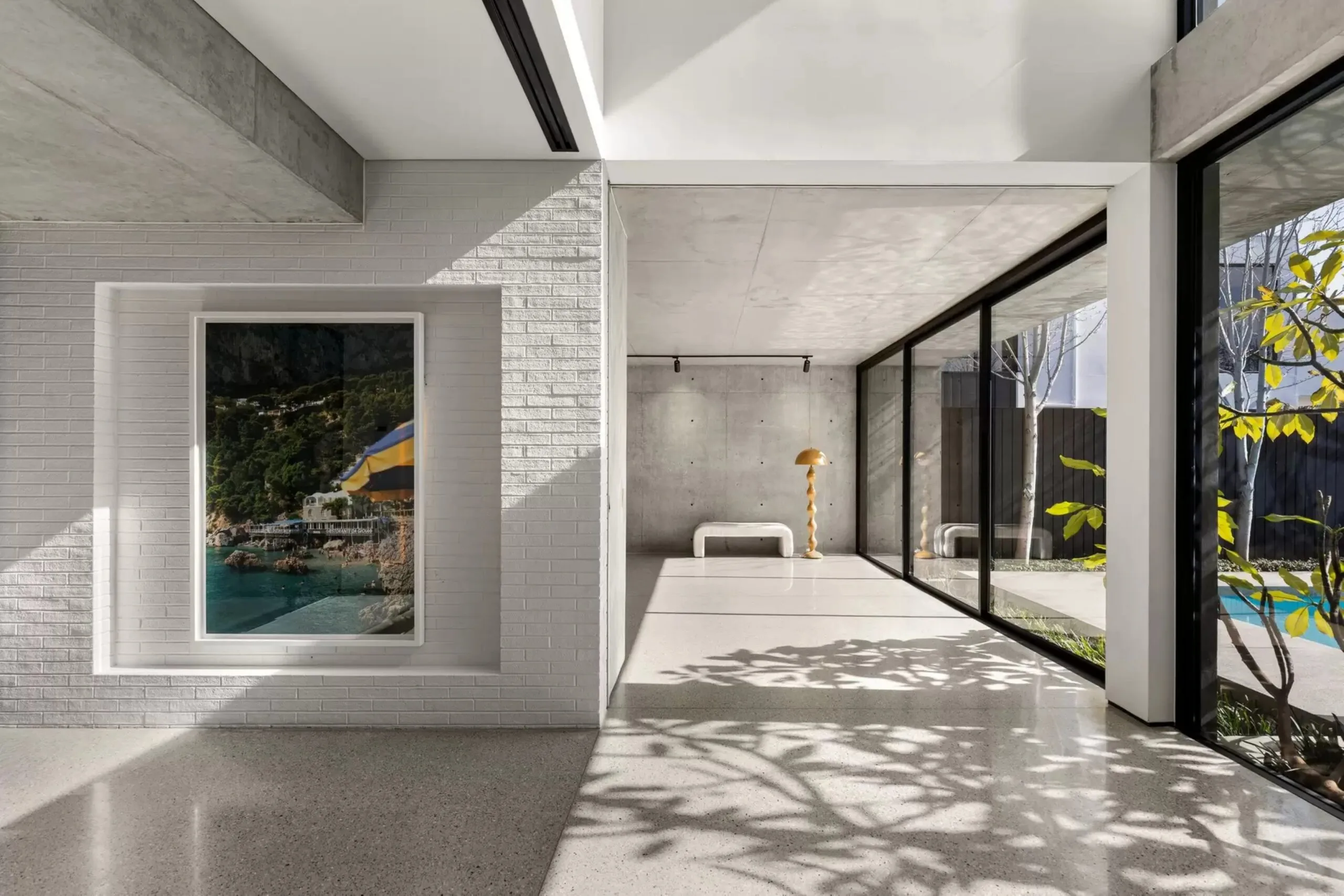 Light-filled interior with polished floors, white brick wall, artwork and floor-to-ceiling windows overlooking the garden.