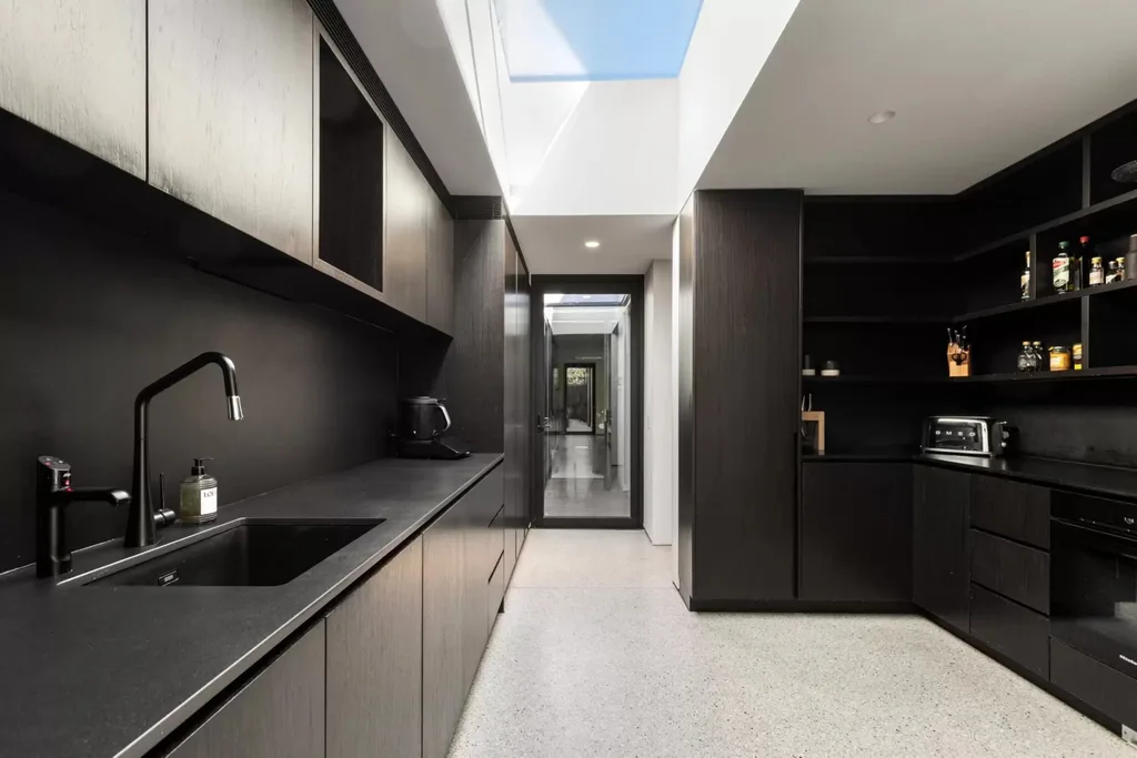 Black butler's pantry with dark cabinetry, sink, open shelving and a large overhead skylight.