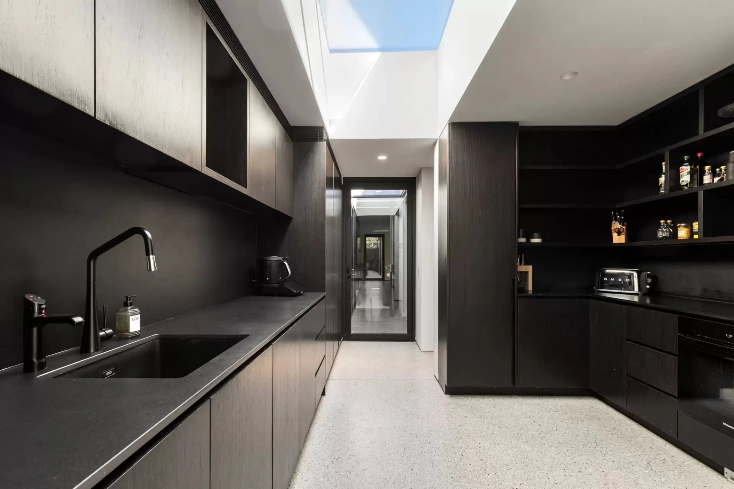 Black butler's pantry with dark cabinetry, sink, open shelving and a large overhead skylight.