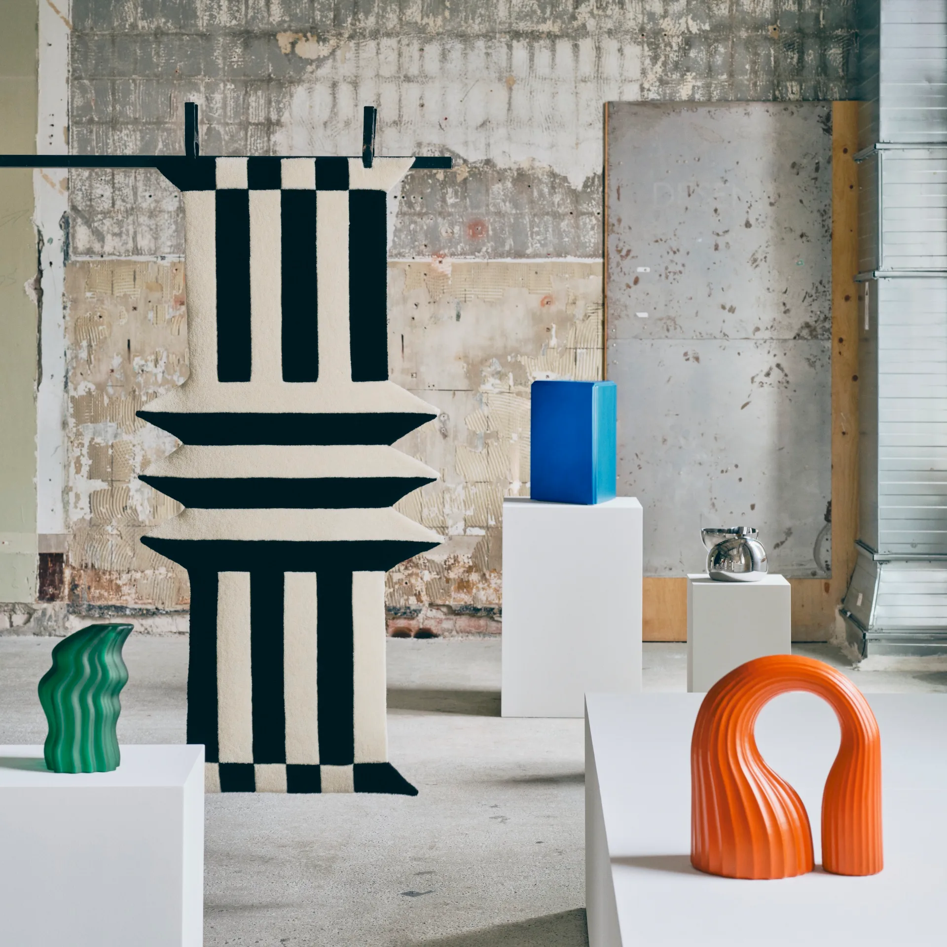 Orange and green sculptural objects, a blue glass piece and a black-and-white graphic textile from IKEA&rsquo;s KONSTRUNDA collection displayed in a gallery